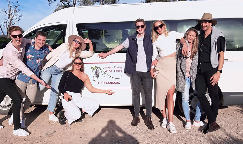 Group of seven young adults smiling and posing in front of a white van with a Mudgee Valley Wine Tours sign on the door.