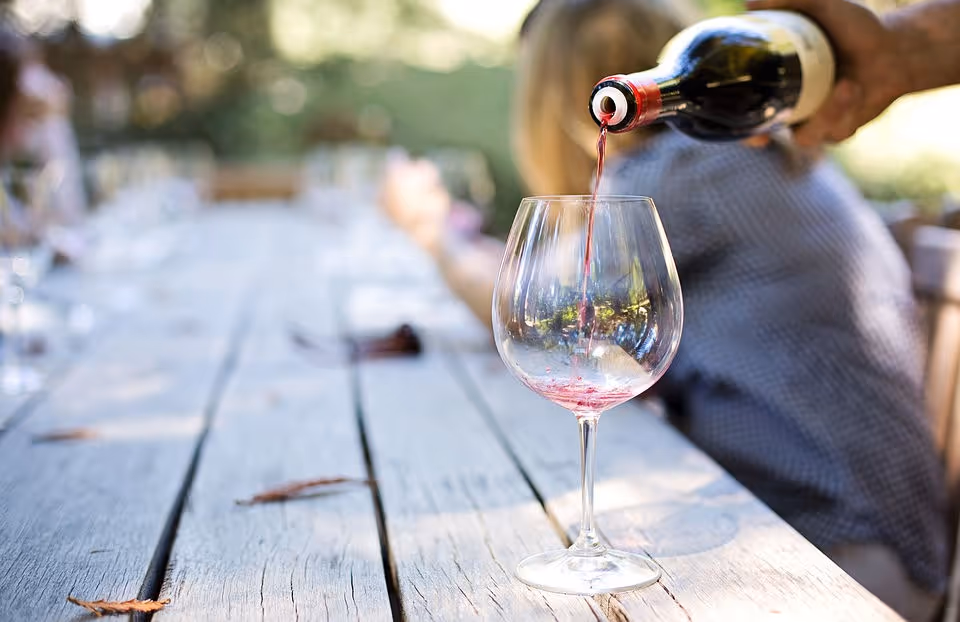 Red wine being poured from a bottle into a glass on a wooden outdoor table.