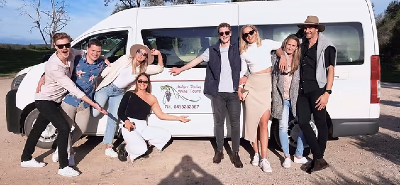 Group of eight smiling people posing in front of a white van with a 'Mudgee Valley Wine Tours' sign on the side.